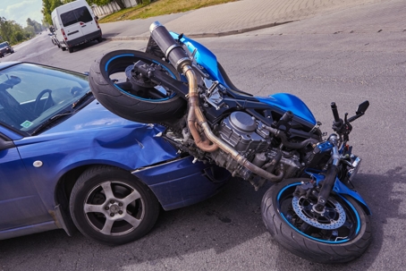 Blue compact car collides with a blue sport motorcycle on a sunny day